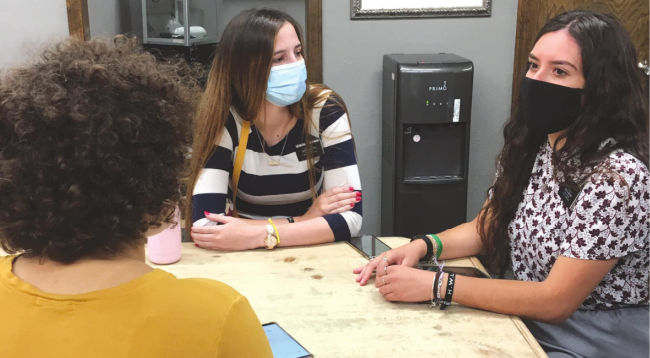 dos hermanas misioneras que enseñan a alguien que está sirviendo en la misión durante el COVID-19 con máscaras