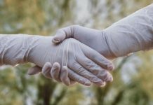 two people shaking hands wearing gloves during covid-19