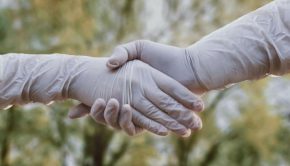 two people shaking hands wearing gloves during covid-19