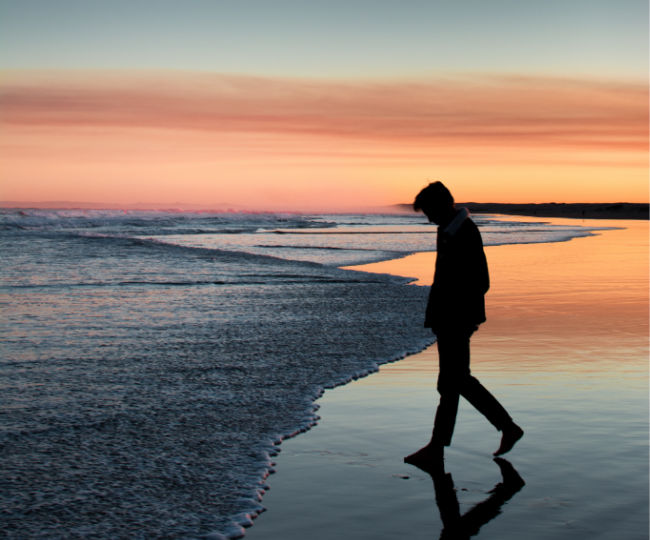 a man walking along the beach at sunset