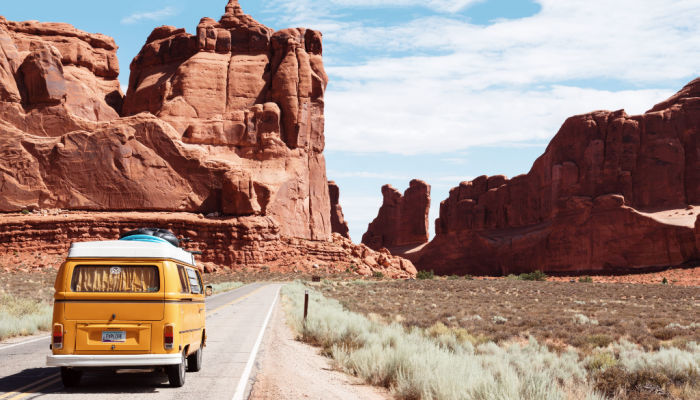 volkswagen bus driving towards red rock on a road trip