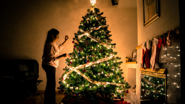 young woman putting lights on christmas tree