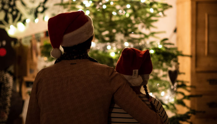 mother and daughter sit together next to a christmas tree while wearing santa hats