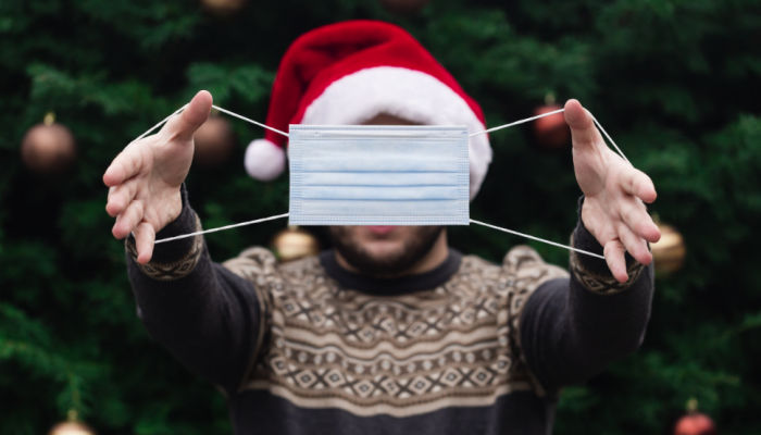 man holding up mask covid-19 christmas wearing a santa hat